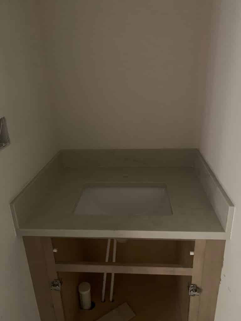 Grey quartz bathroom vanity countertop with an undermount sink, installed above an unfinished cabinet
