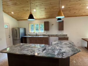 Kitchen island with dramatic granite countertop beneath a vaulted wood-plank ceiling