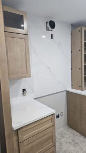 White quartz countertop and matching full-height backsplash with soft grey veining in a light wood kitchen