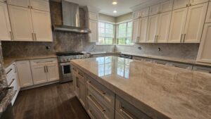 White kitchen cabinets with brass hardware and taupe veined stone countertops and backsplash