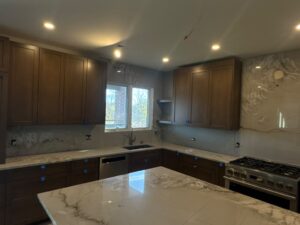 Wide view of a kitchen with a veined stone island countertop, full-height backsplash, and dark wood cabinetry