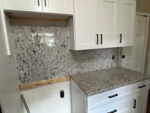 Close-up of a speckled granite countertop and matching backsplash in a white cabinet kitchen
