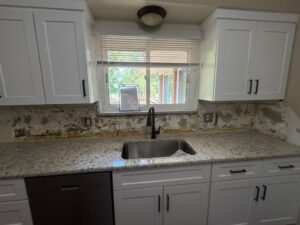 Speckled granite countertop and sink installed in a white kitchen with the backsplash wall prepped for finishing