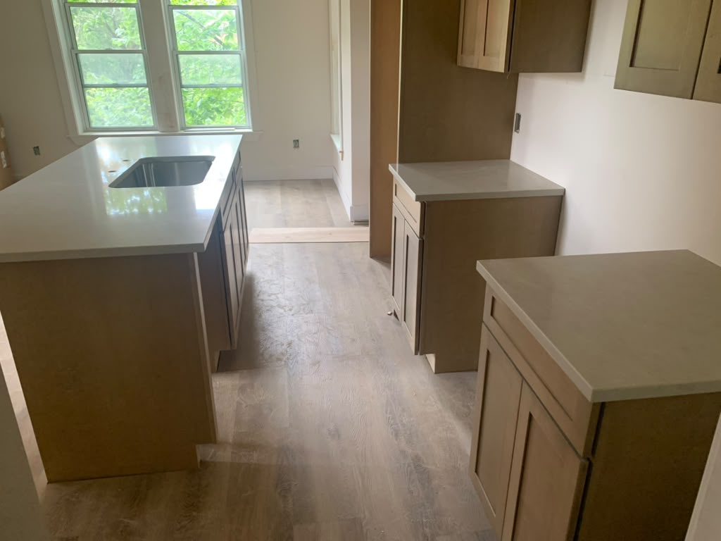 Light grey quartz countertops on a kitchen island and perimeter cabinets with light wood cabinetry
