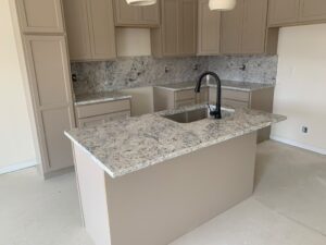 Kitchen island countertop with white and grey speckled granite and matching backsplash in a new build