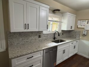 White cabinet kitchenette with a speckled granite countertop, black hardware, and a stainless dishwasher