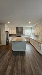 White cabinet kitchen with a grey stone island and matching perimeter countertops beneath a stainless range hood