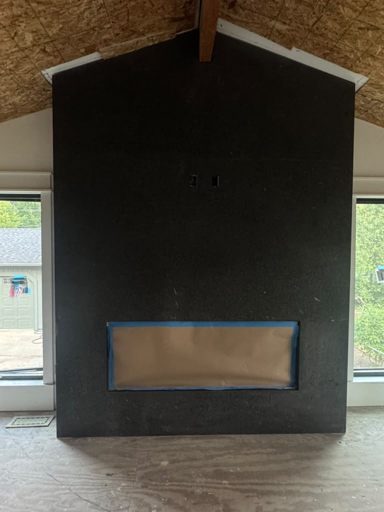 Floor to ceiling black stone fireplace surround under a vaulted wood ceiling