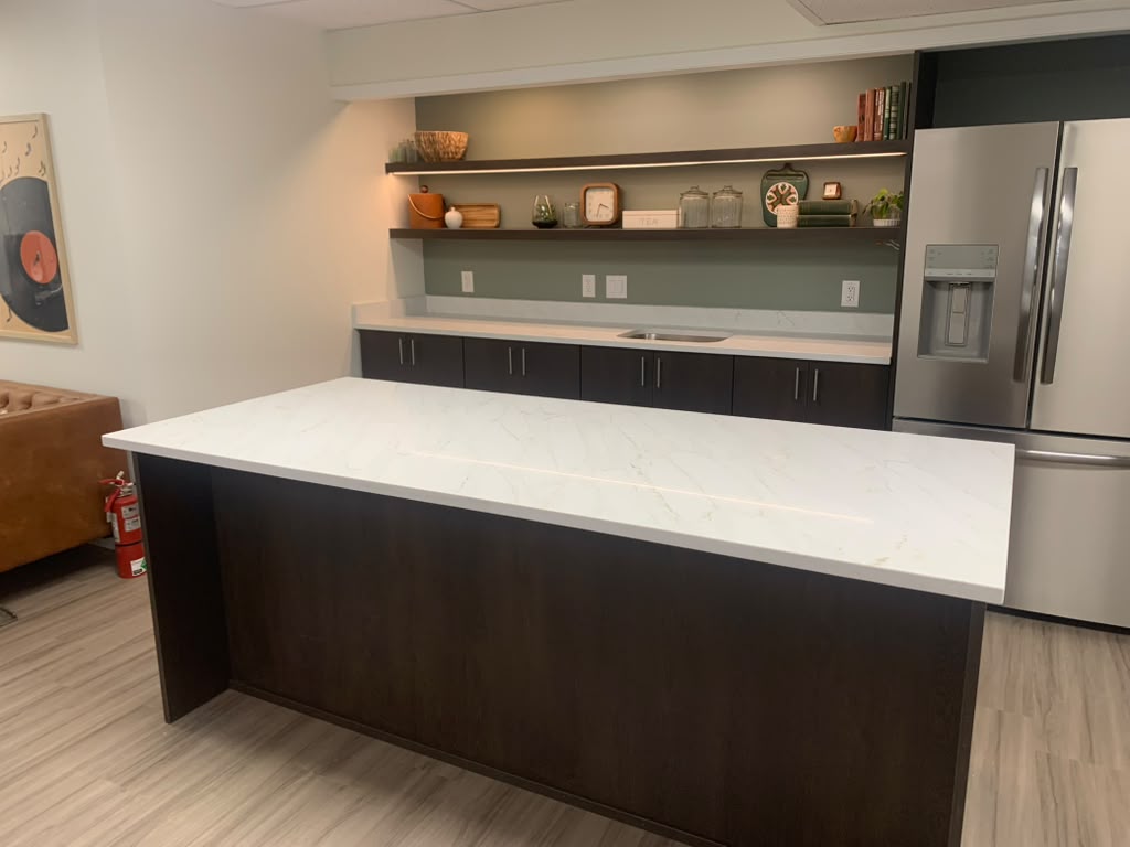 White stone island countertop with waterfall edge next to a built-in stainless steel refrigerator